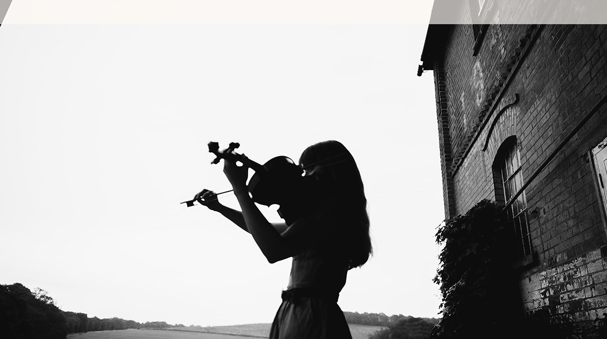 Lady playing violin looking out onto countryside