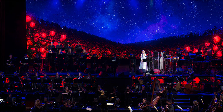 Lady in white dress singing on stage with an orchestra all around her
